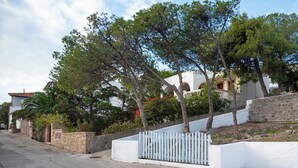 Zona residencial com um edifício branco, muros de pedra e entrada com portão.