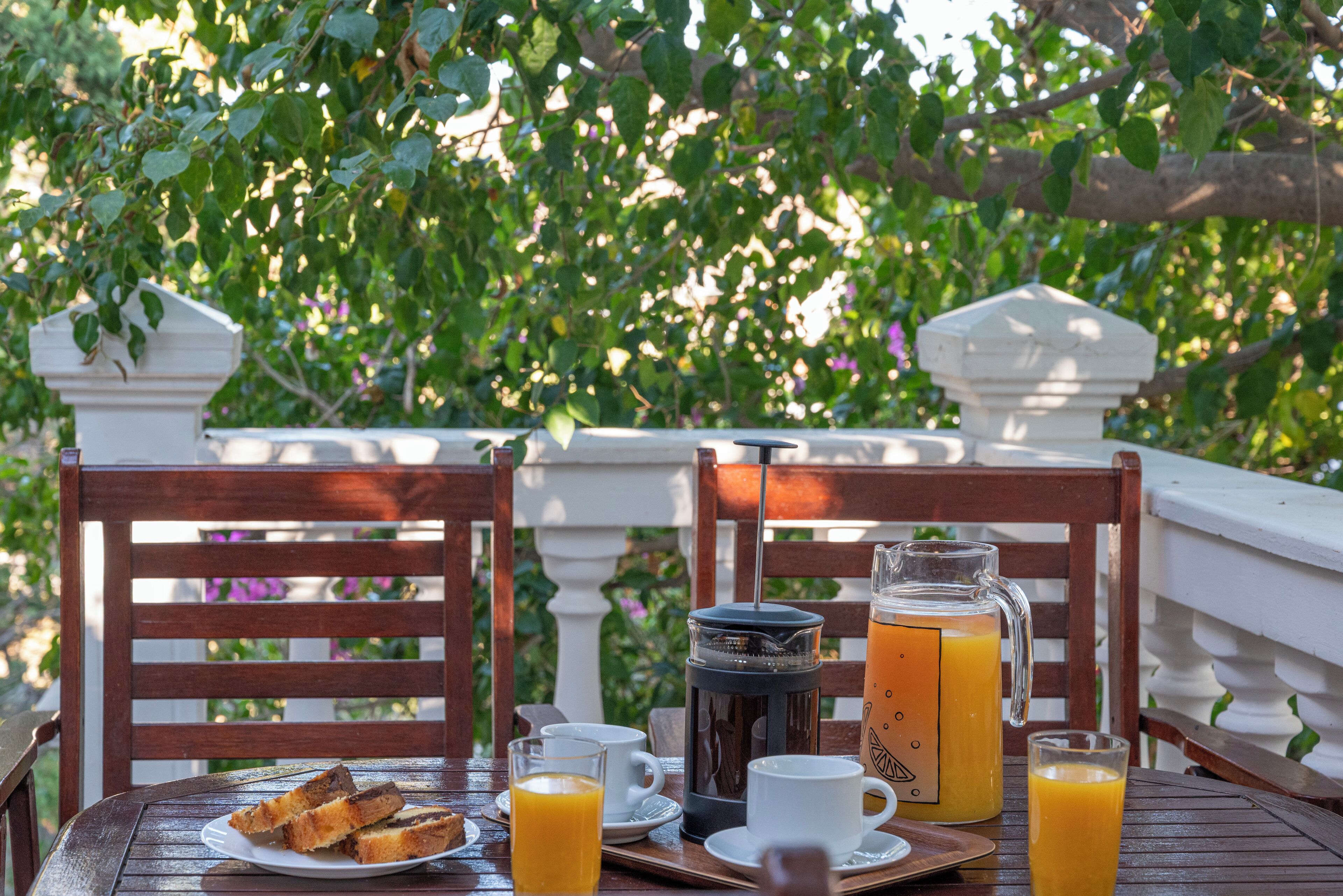 Une table en bois dressée pour le petit-déjeuner, avec une assiette de toasts, une cafetière et un verre de jus d’orange.