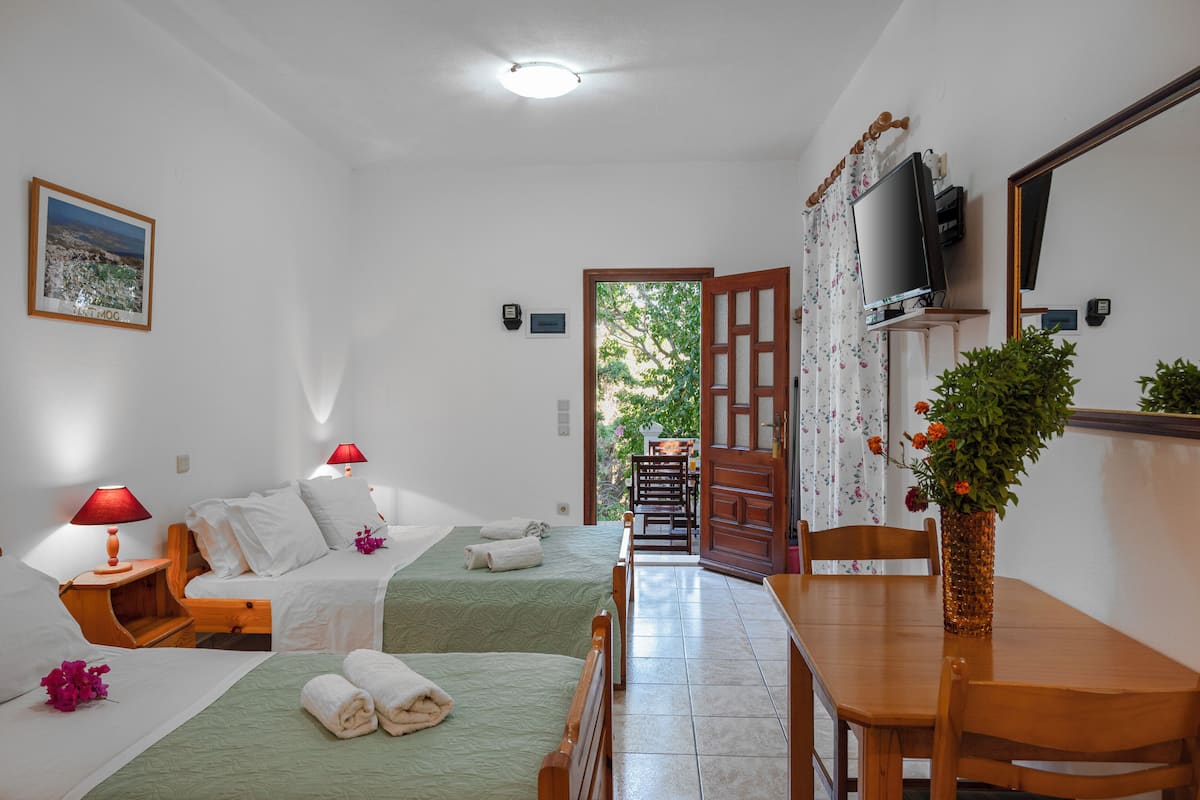 A hotel room with two beds, a wooden table, a TV, and a view of the outdoors.