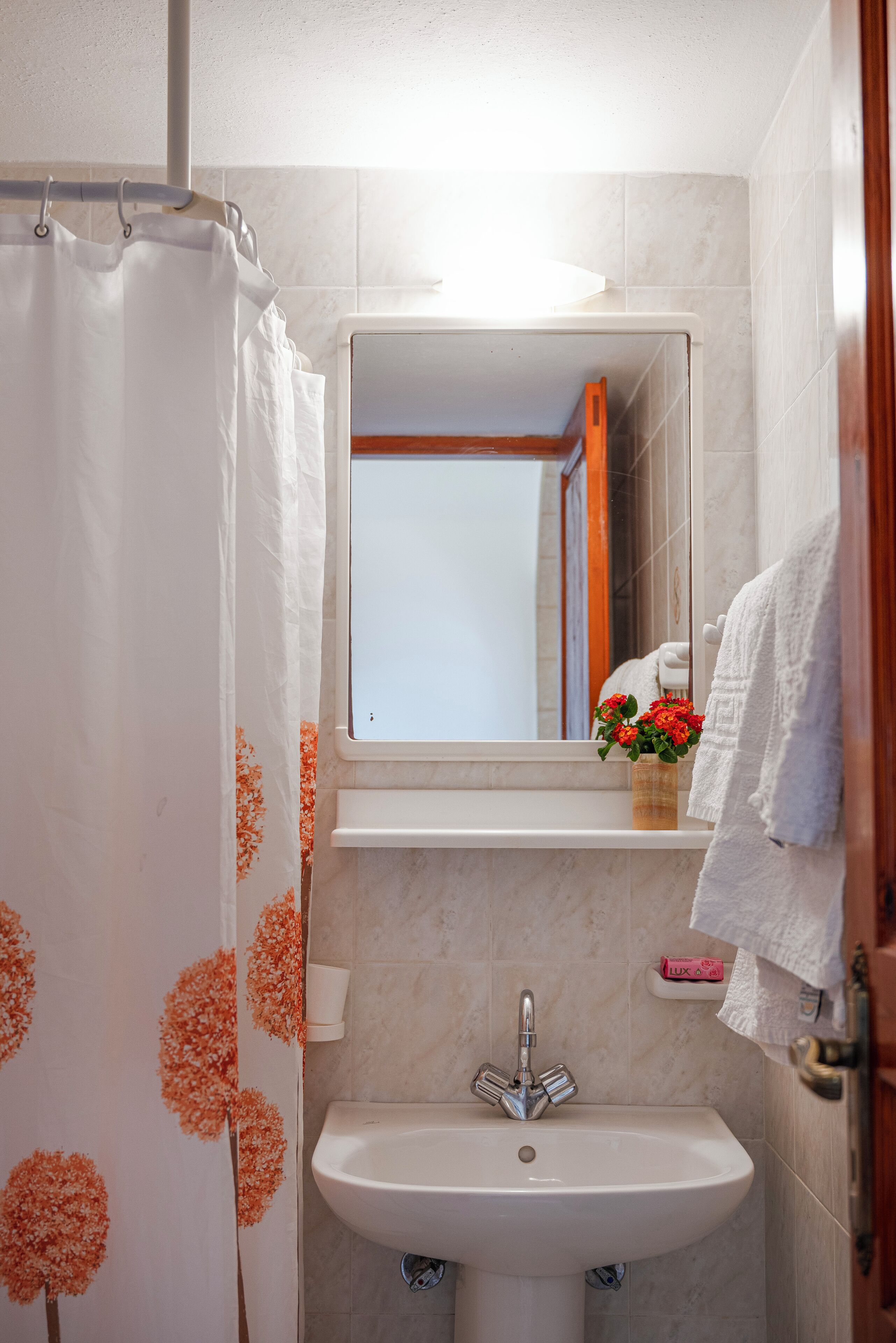 A bathroom with a white sink, a mirror, and a shower curtain with orange floral patterns.