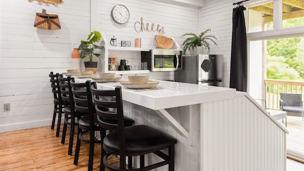 Una cocina moderna con una isla blanca, sillas negras y vistas al exterior.