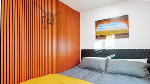 Une chambre moderne avec un mur en lambris de bois, un lit avec une literie aux tons gris et jaune, et un tableau représentant un paysage accroché au mur.