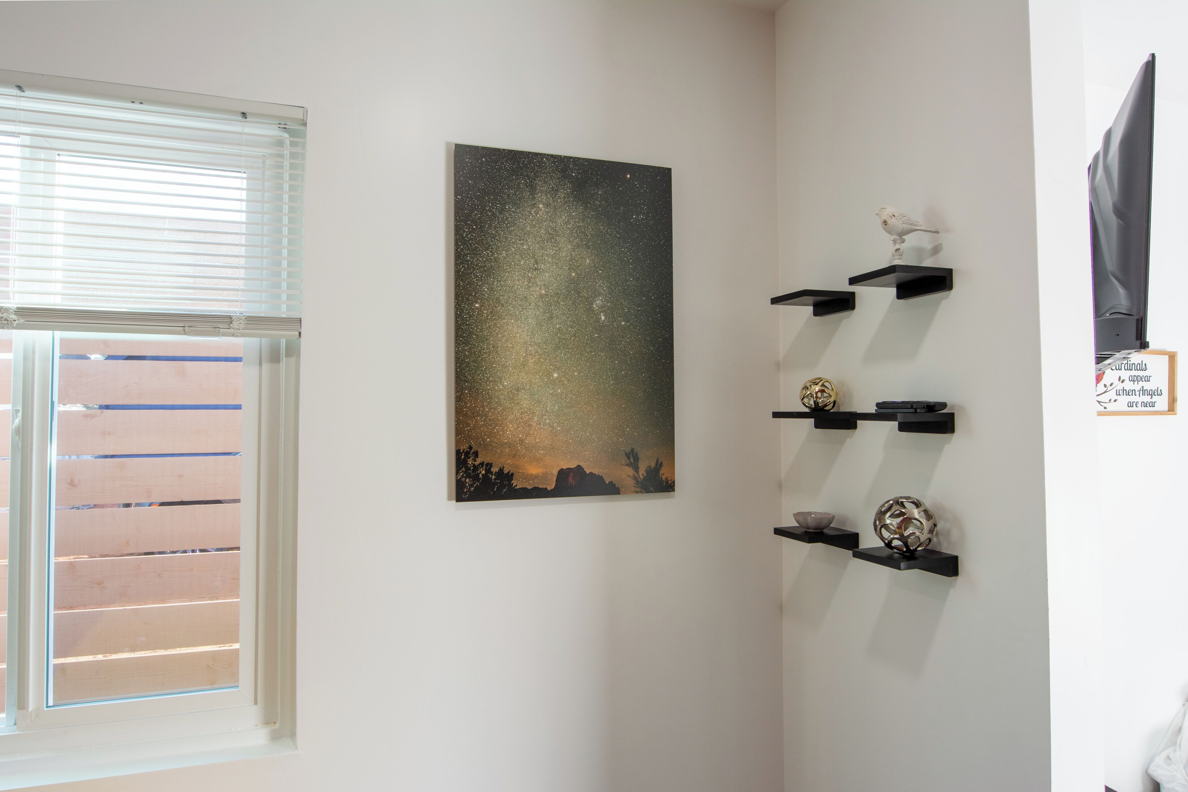 A room with a starry night sky painting, a window with blinds, and shelves with decorative items.