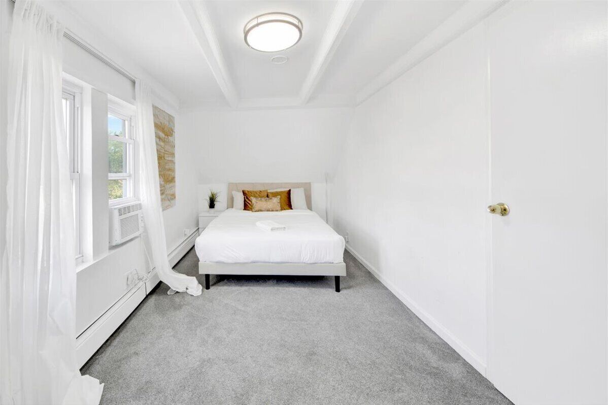 A bedroom with a bed, a window with curtains, a radiator, and a door.