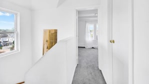 A hallway with white walls, a wooden accent wall, a carpeted floor, and a door with a brass handle. - Two Wash (Yonkers)