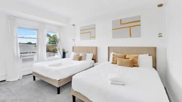 Habitación de hotel con dos camas, ropa blanca de cama, vista a través de un ventanal grande y arte abstracto en la pared.