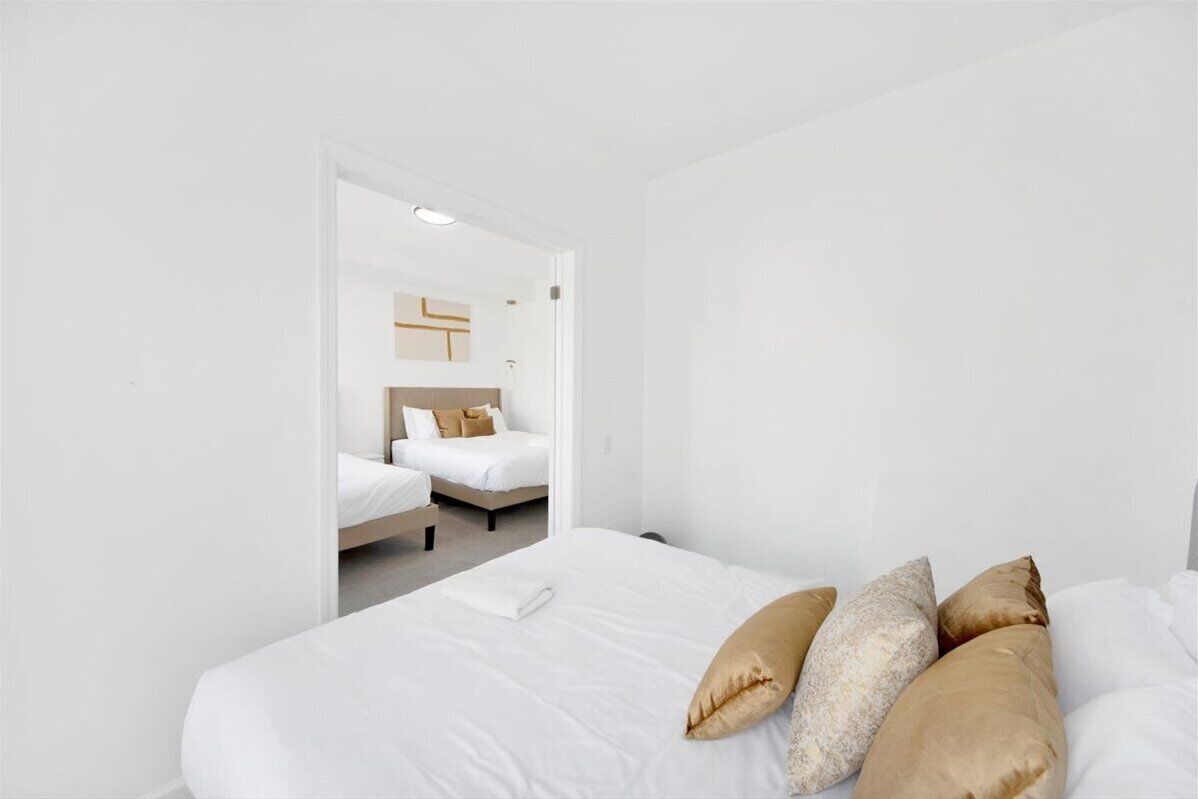 Habitación de hotel con una cama grande, una cama más pequeña al fondo y una puerta blanca que conduce a otra habitación.