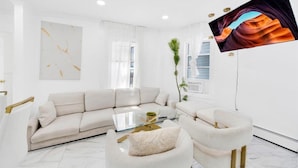 A modern living room with a sectional sofa, a glass coffee table, and a large flat-screen TV mounted on the wall. - Two Wash (Yonkers)