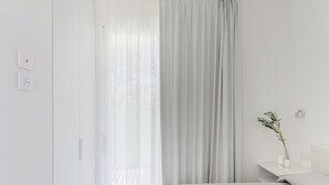 A minimalist bedroom with a bed, a nightstand, a vase with a plant, and sheer curtains. - Charmant Apartment Near La Pelosa Beach (Stintino)