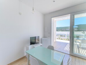 A modern room with a glass table, white chairs, a flat-screen TV, and a view of a balcony with outdoor furniture. - Charmant Apartment Near La Pelosa Beach (Stintino)