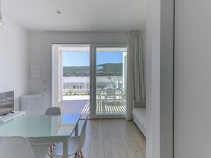 Una habitación moderna con una mesa y sillas de vidrio, un sofá y un ventanal corredero que da a un patio exterior con vistas a una colina.
