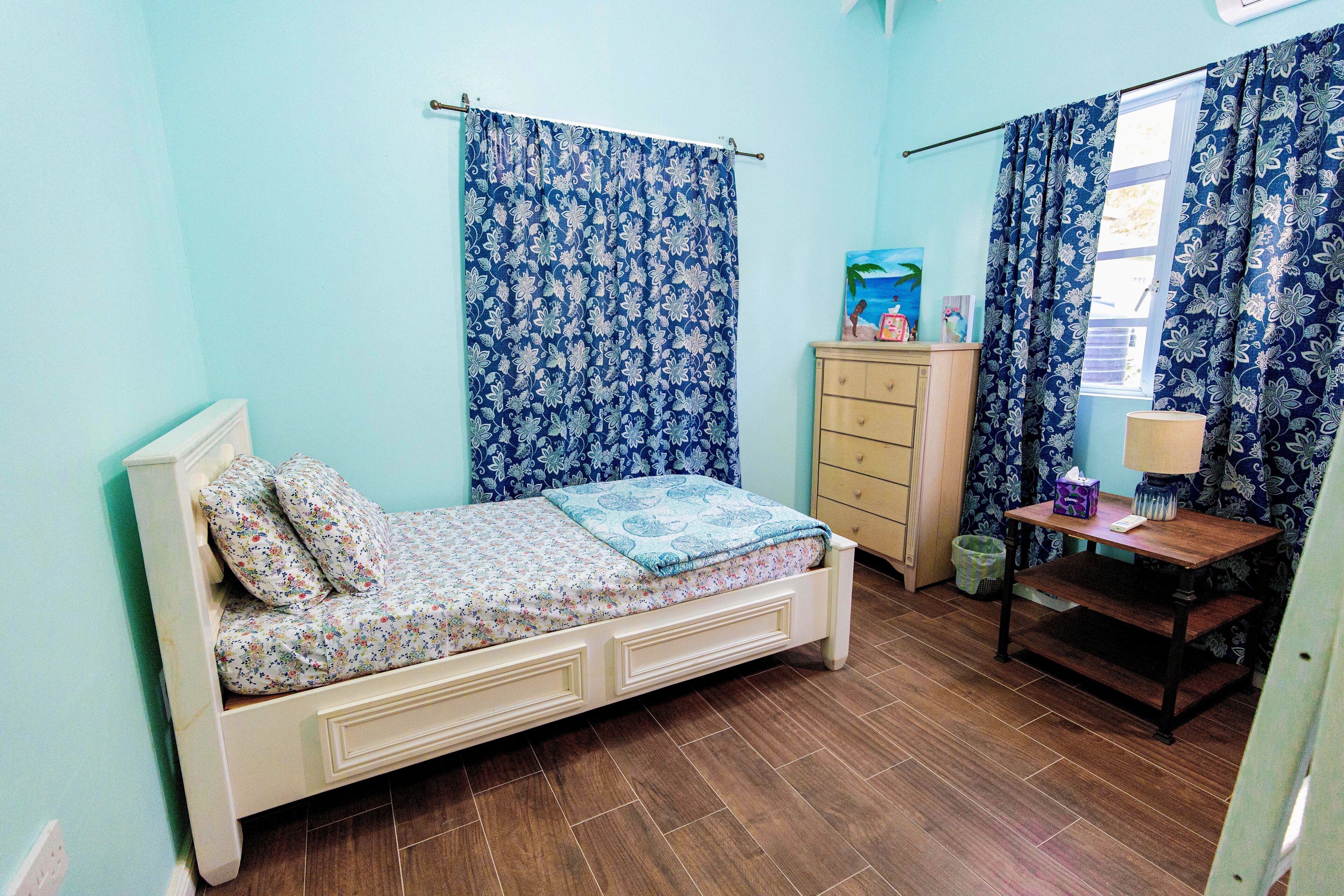 Une chambre à coucher avec un lit, une commode, une table de chevet et une fenêtre avec des rideaux.