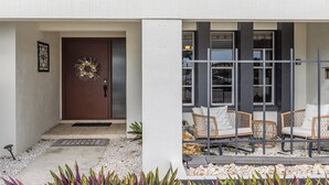 Un edificio moderno con una puerta marrón, un adorno de corona y una zona de estar con mobiliario de mimbre.