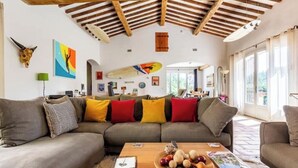 A spacious living room with a wooden ceiling, a large sofa, and a coffee table with various items. - Magnificent villa with swimming pool and view of Saint Paul de Vence (Saint-Paul-de-Vence)
