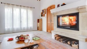 A living room with a fireplace, a wooden table with fruit, and a bookshelf. - Magnificent villa with swimming pool and view of Saint Paul de Vence (Saint-Paul-de-Vence)
