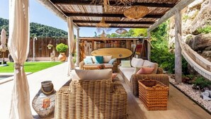 A covered outdoor seating area with wicker furniture, a wooden table, and a hammock. - Magnificent villa with swimming pool and view of Saint Paul de Vence (Saint-Paul-de-Vence)