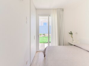 Ein Schlafzimmer mit einem Bett, einem Nachttisch, einem Fenster mit Vorhängen und Blick auf einen Garten.