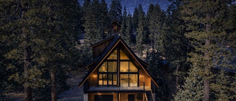 Une cabane dotée d’une grande baie vitrée, d’une terrasse en bois et d’un garage.