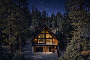 Une cabane dotée d’une grande baie vitrée, d’une terrasse en bois et d’un garage.