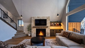 Una amplia sala de estar con chimenea de piedra, un conjunto de sofás cómodos y una escalera que conduce a un nivel superior.