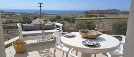 A balcony with a sofa, chairs, a table, and a view of the sea.