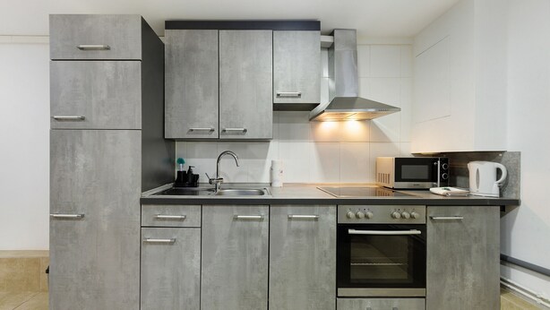 Een moderne keuken met grijze kastjes, een roestvrijstalen afzuigkap, een magnetron en een inbouwoven.