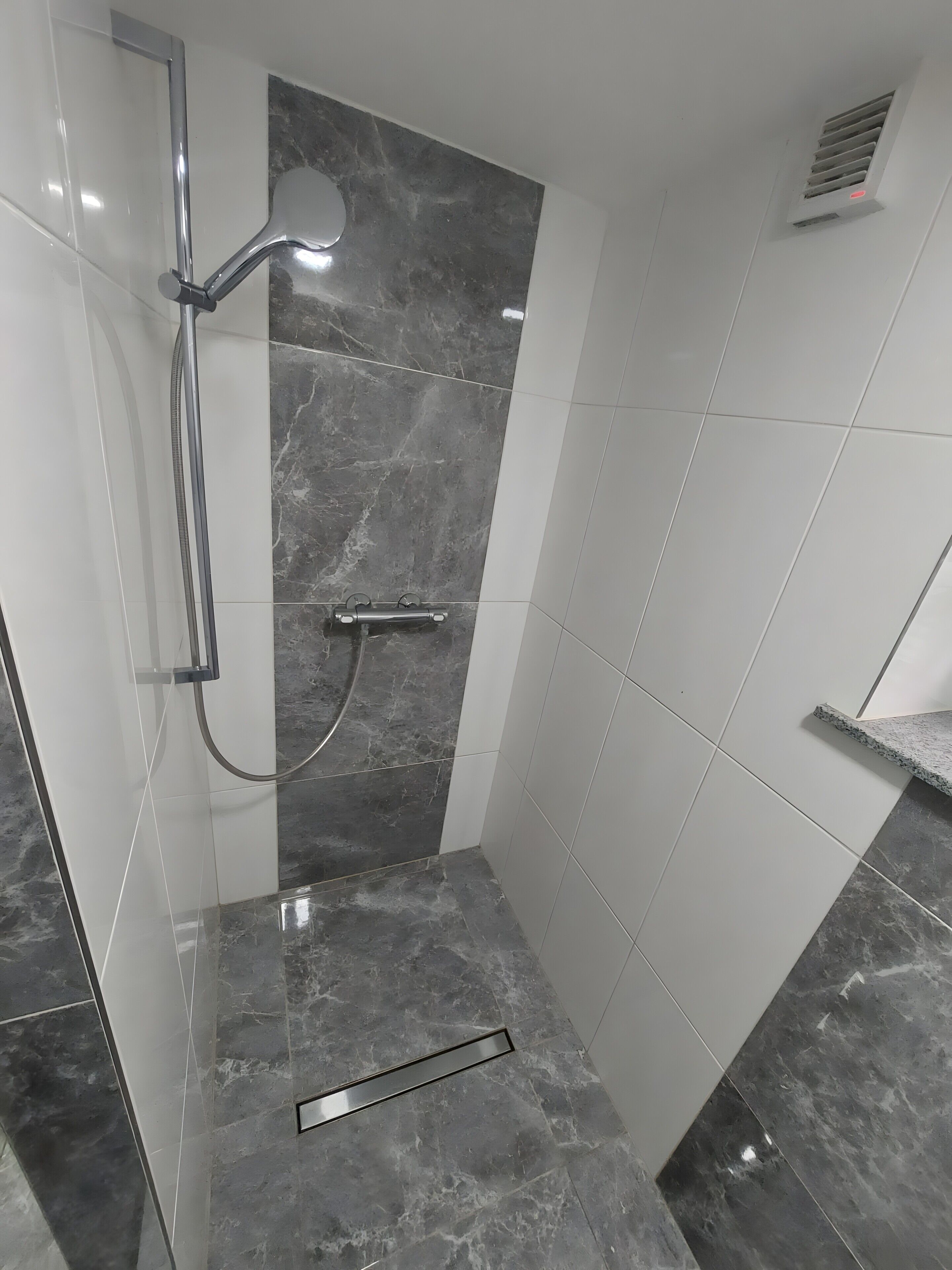 A bathroom with a shower, a handrail, and a tiled floor.