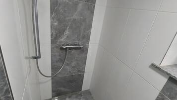 A bathroom with a shower, a handrail, and a tiled floor.