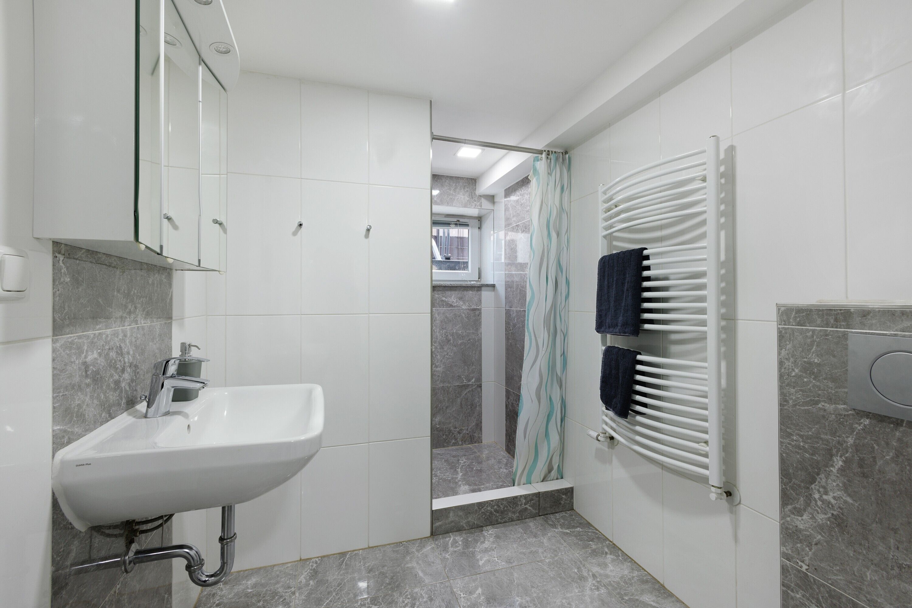 Un baño con lavamanos, espejo, ducha y toallero.