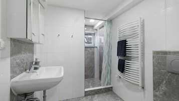 Un baño con lavamanos, espejo, ducha y toallero.