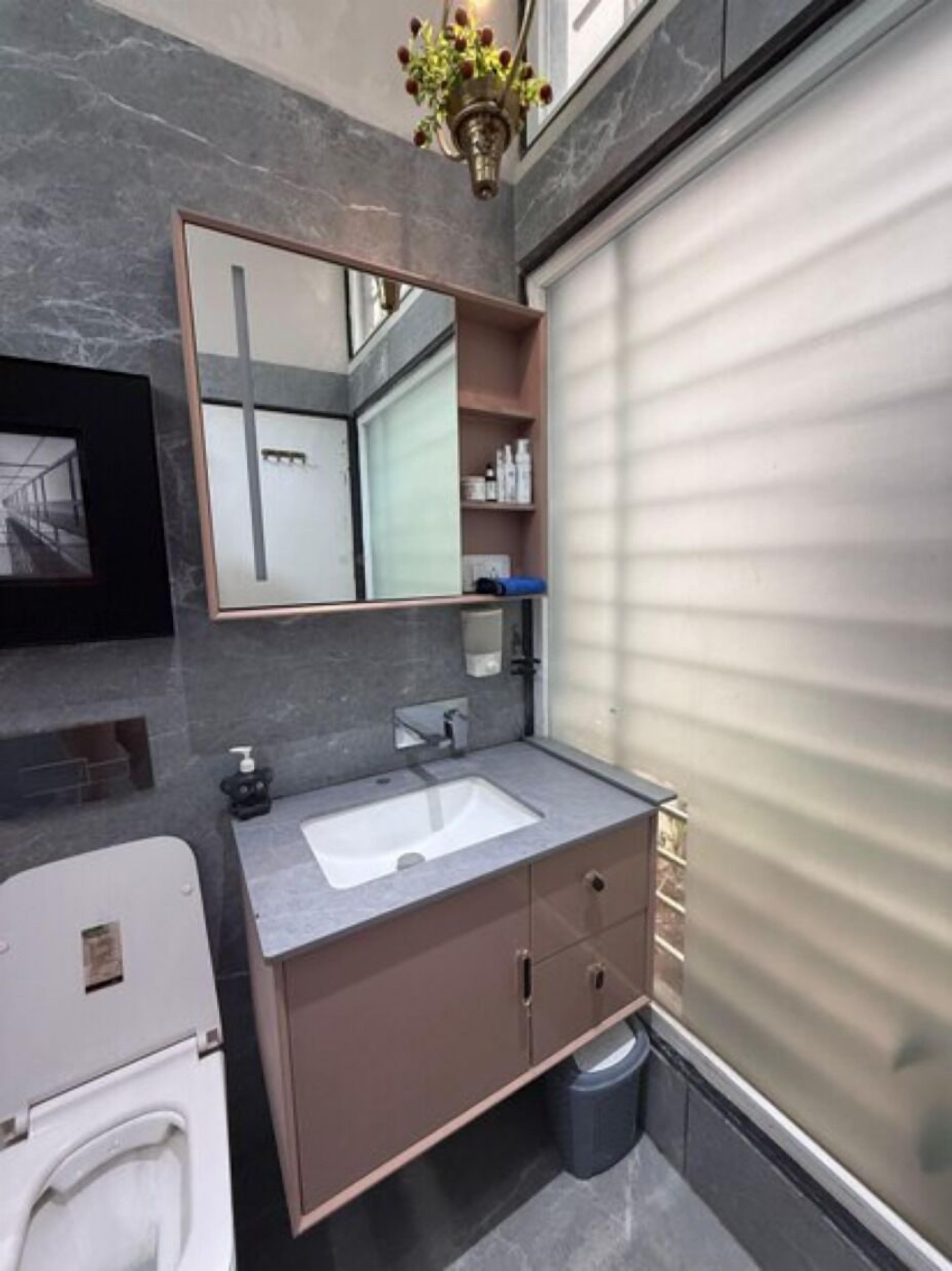 A modern bathroom with a grey marble wall, a large mirror, a white sink, and a built-in toilet.