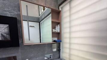 A modern bathroom with a grey marble wall, a large mirror, a white sink, and a built-in toilet.