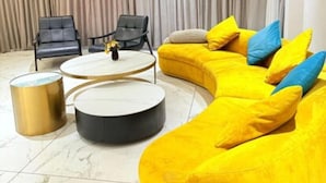 Un salon moderne avec un canapé d’angle jaune, deux fauteuils et une table basse ronde.