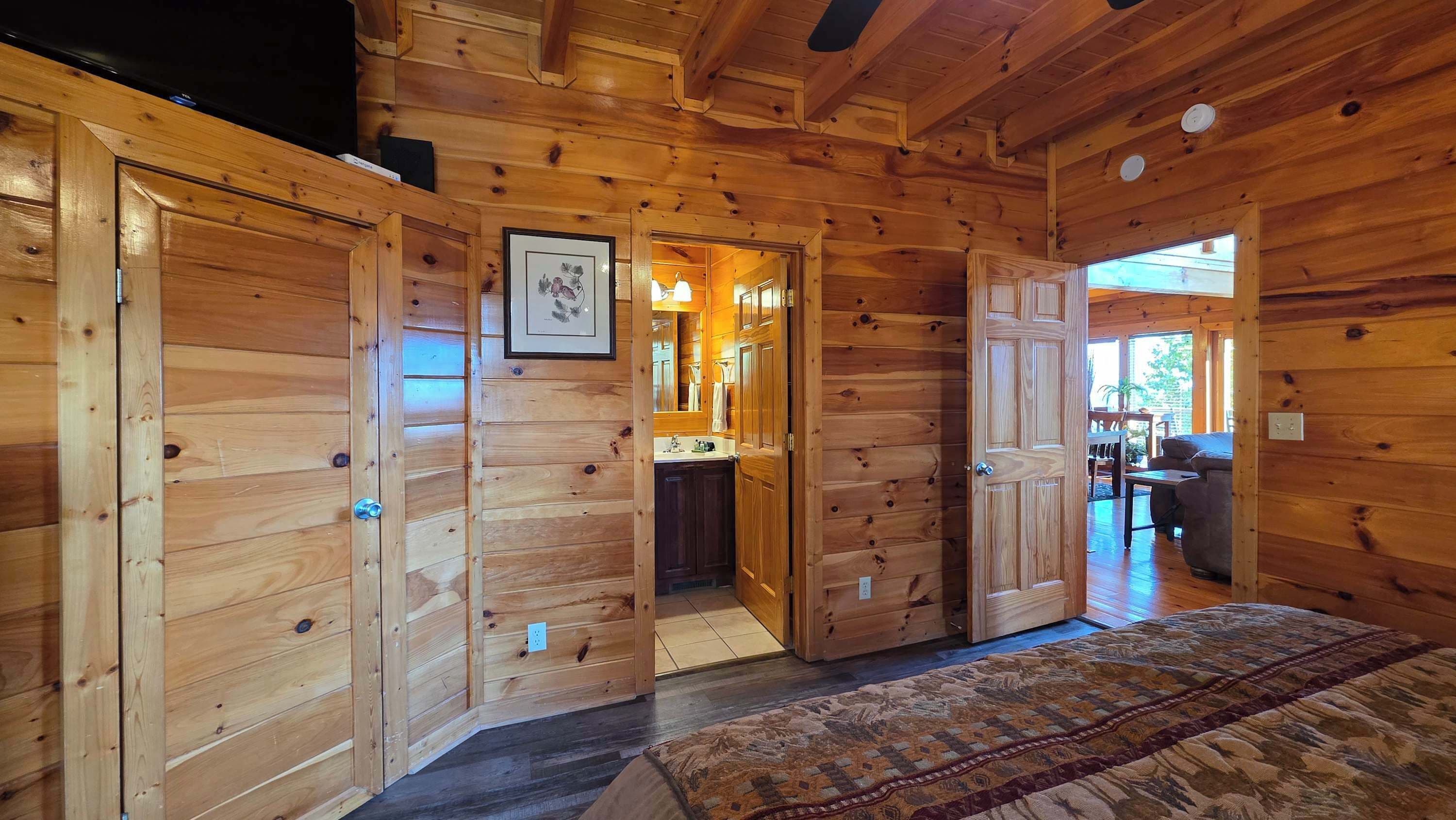 Interior de una cabaña de madera con una cama grande, un baño con lavabo y un comedor con mesa y sillas.