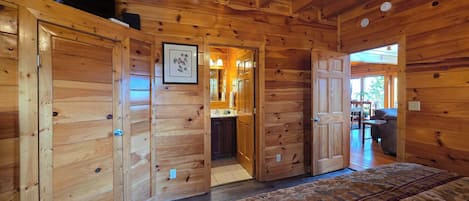 A wooden cabin interior with a large bed, a bathroom with a sink, and a dining area with a table and chairs.