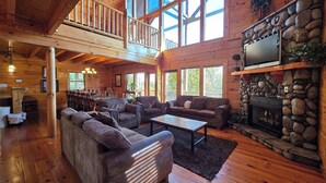 A spacious wooden cabin with a dining area, a living room with a fireplace, and a balcony. - Spacious Cabin, Sleep 28, Hot Tub, Games, Shared Pool (Pigeon Forge)