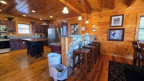A wooden cabin interior with a kitchen, dining area, and bar. - Spacious Cabin, Sleep 28, Hot Tub, Games, Shared Pool (Pigeon Forge)