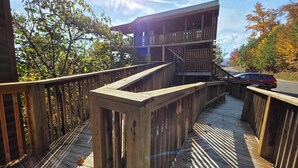 A wooden deck with a staircase leading to a multi-level building. - Spacious Cabin, Sleep 28, Hot Tub, Games, Shared Pool (Pigeon Forge)