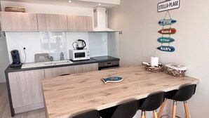 Une cuisine moderne avec un îlot central en bois, des tabourets de bar noirs et un panneau mural portant l’inscription « STELLA-PLAGE ».