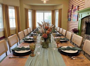 A long dining table set for a formal meal with chairs, a vase with flowers, and a fireplace. - Desert Playground | Pool, Cold Plunge & Arcade (Mesa)