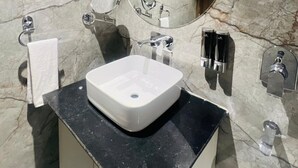A bathroom with a marble wall, a large mirror, a white sink, and a towel rack. - HOTEL SUPREME INN (Varanasi)