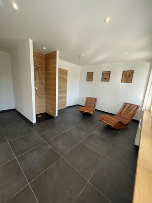 A modern bathroom with dark tiles, a wooden shower enclosure, and two wooden lounge chairs. - Gîte VALART house 550m2 with Jacuzzi, Sauna, Billiards, Table soccer, darts,... (Le Thillot)