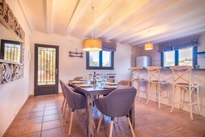 A dining area with a wooden table set for four, surrounded by chairs, and a kitchen area with bar stools. - Rural house on the edge of the Verde river (Tibi)