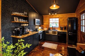 A compact kitchen with dark cabinetry, a coffee machine, a sink, and a refrigerator. - Stonara • Lovers’Hideaway: Cliffside Hot Tub + Sauna + Cinema (Blue Ridge)