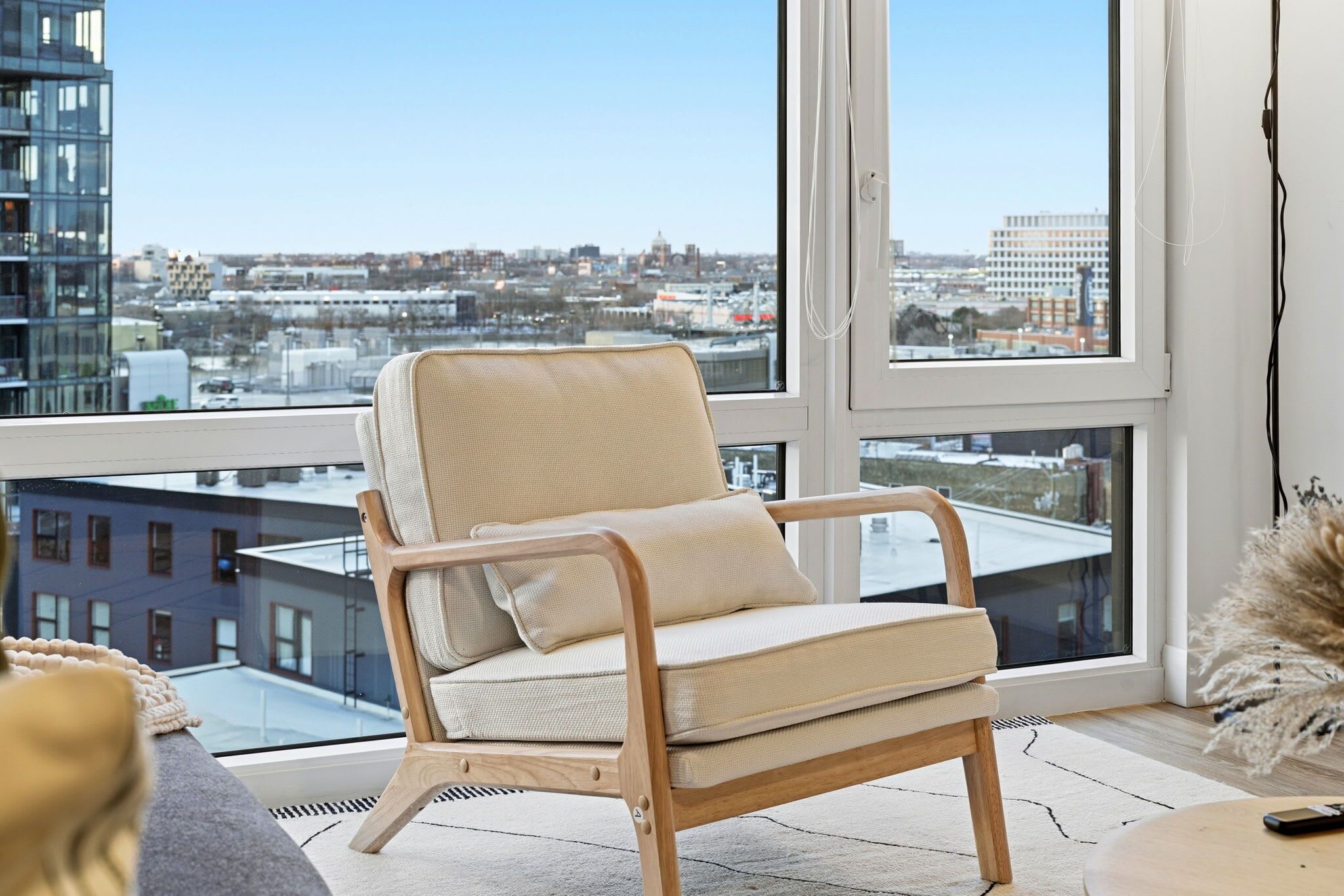 Un fauteuil moderne doté d’un siège et d’un dossier rembourrés, placé devant une grande fenêtre offrant une vue sur le paysage urbain.
