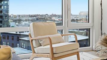Un fauteuil moderne doté d’un siège et d’un dossier rembourrés, placé devant une grande fenêtre offrant une vue sur le paysage urbain.
