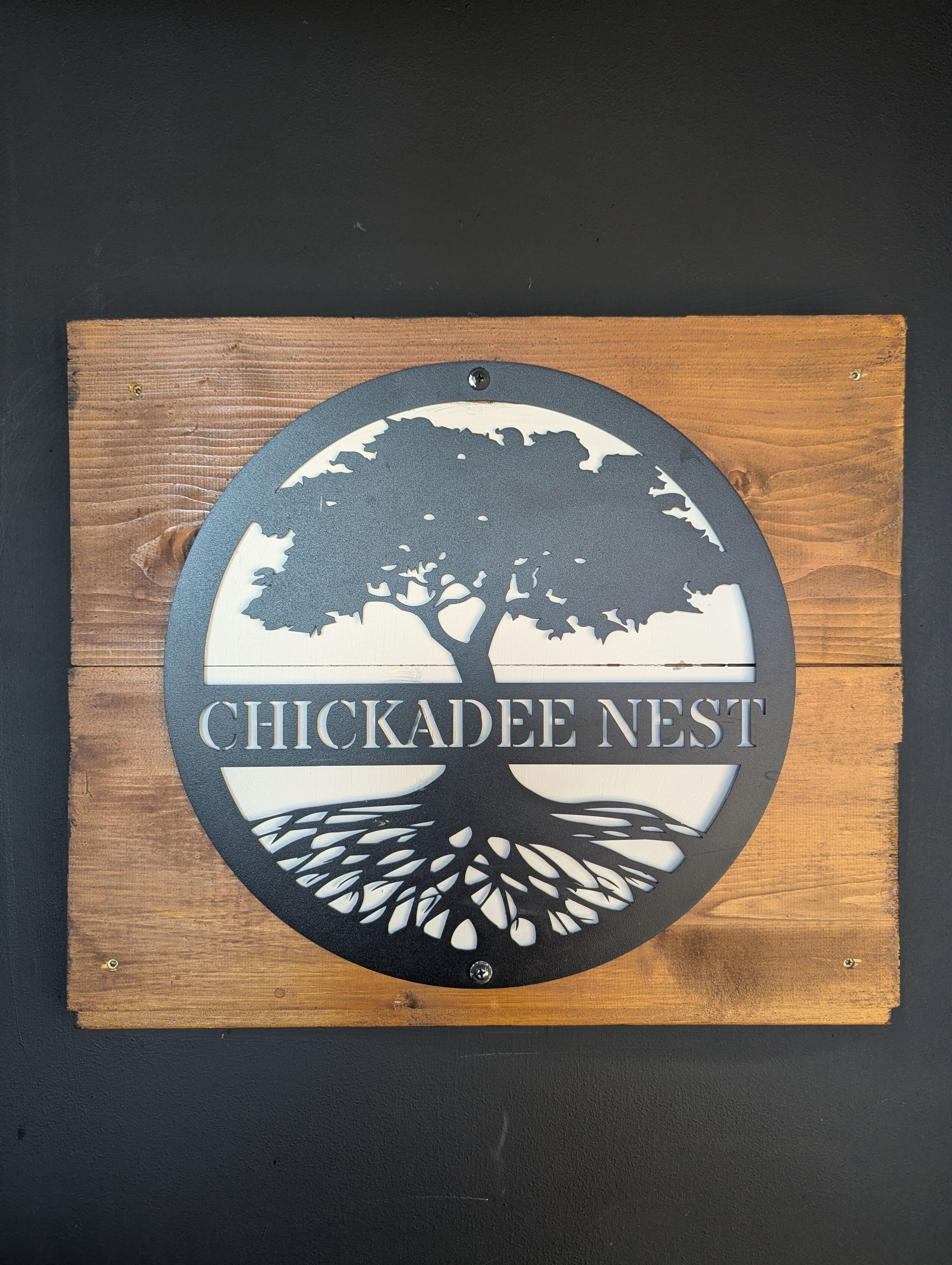 A circular sign with a tree and the text "CHICKADEE NEST" on a wooden background.