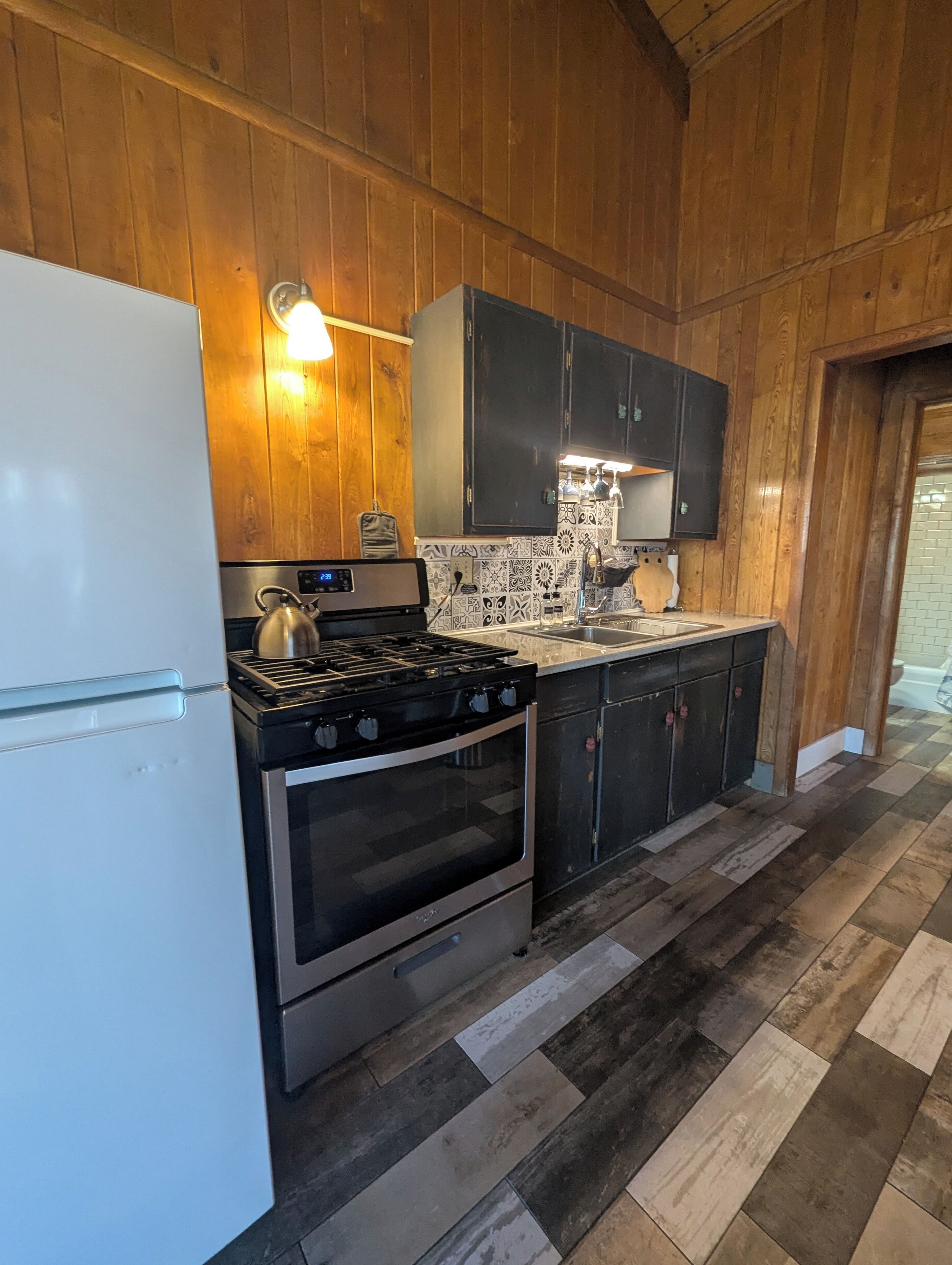 A kitchen with wooden walls, a white refrigerator, a stove, and black cabinets.