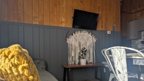 A cozy room with a grey sofa, a wooden accent wall, a macrame wall hanging, a small table with a potted plant, and a white chair. - Feather Nest Inn (Grand Marais)