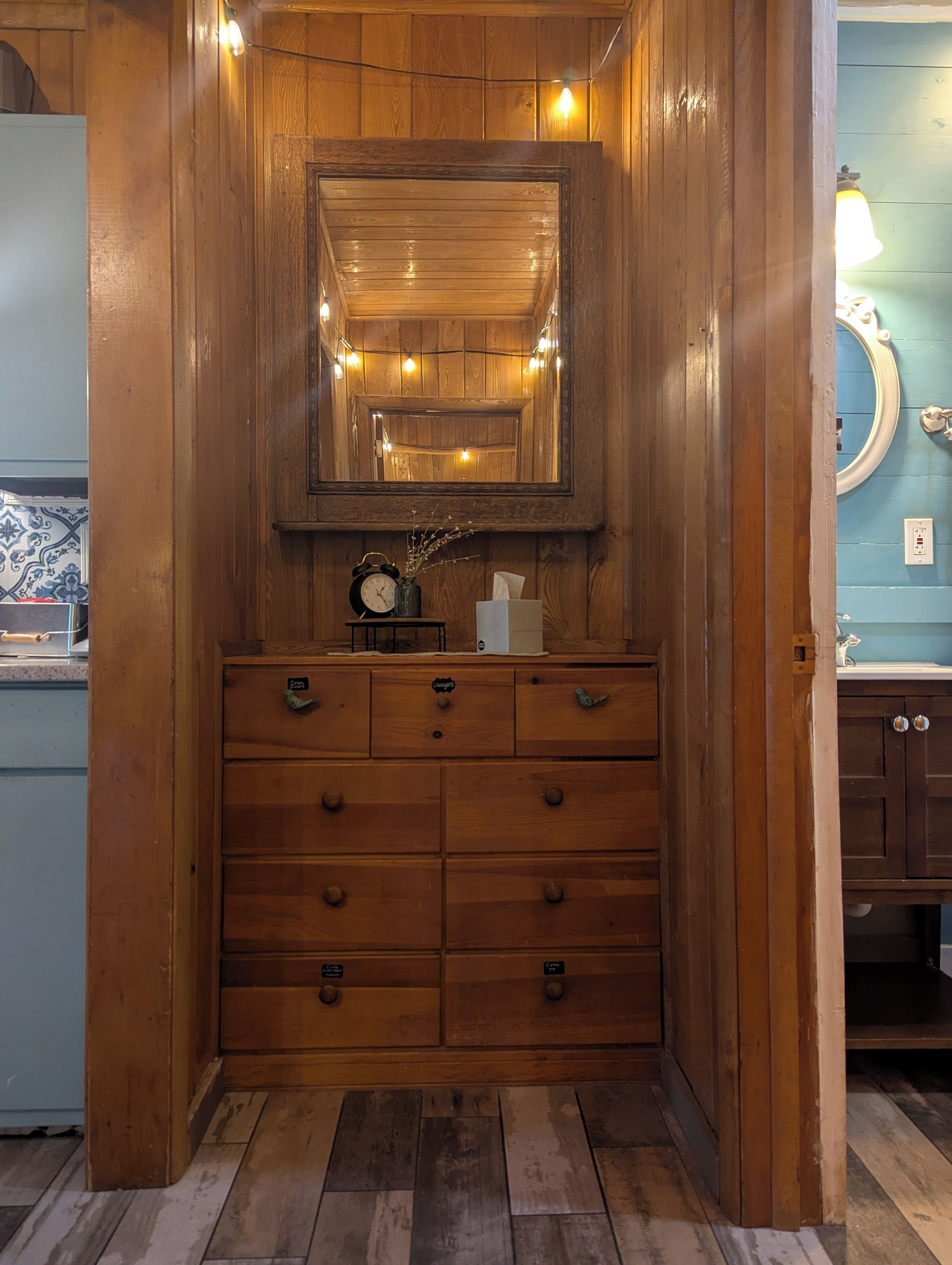 A wooden dresser with a mirror above it, a clock, and a vase with branches.